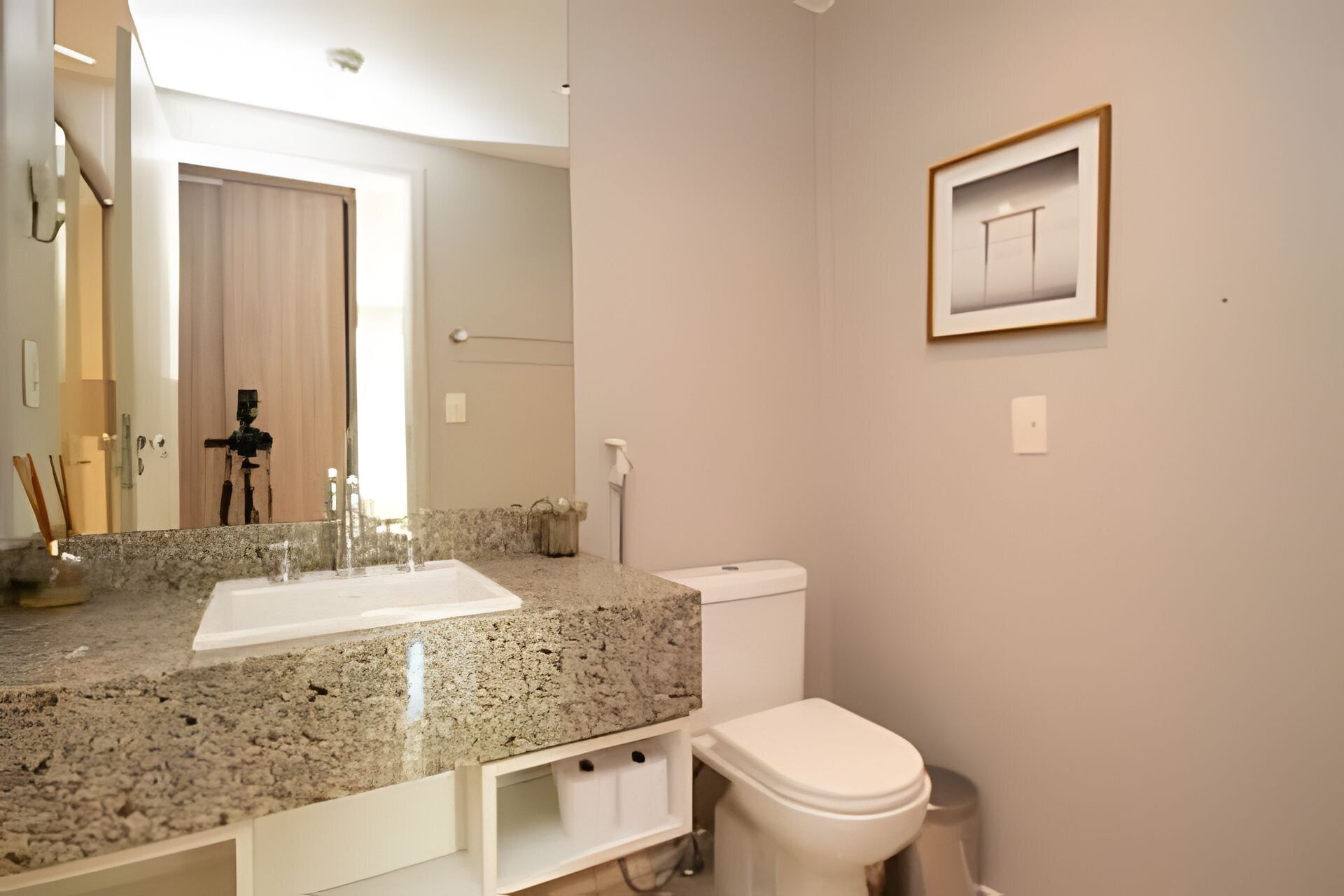 A bathroom with a granite countertop, a white sink, a toilet, and a framed picture on the wall.