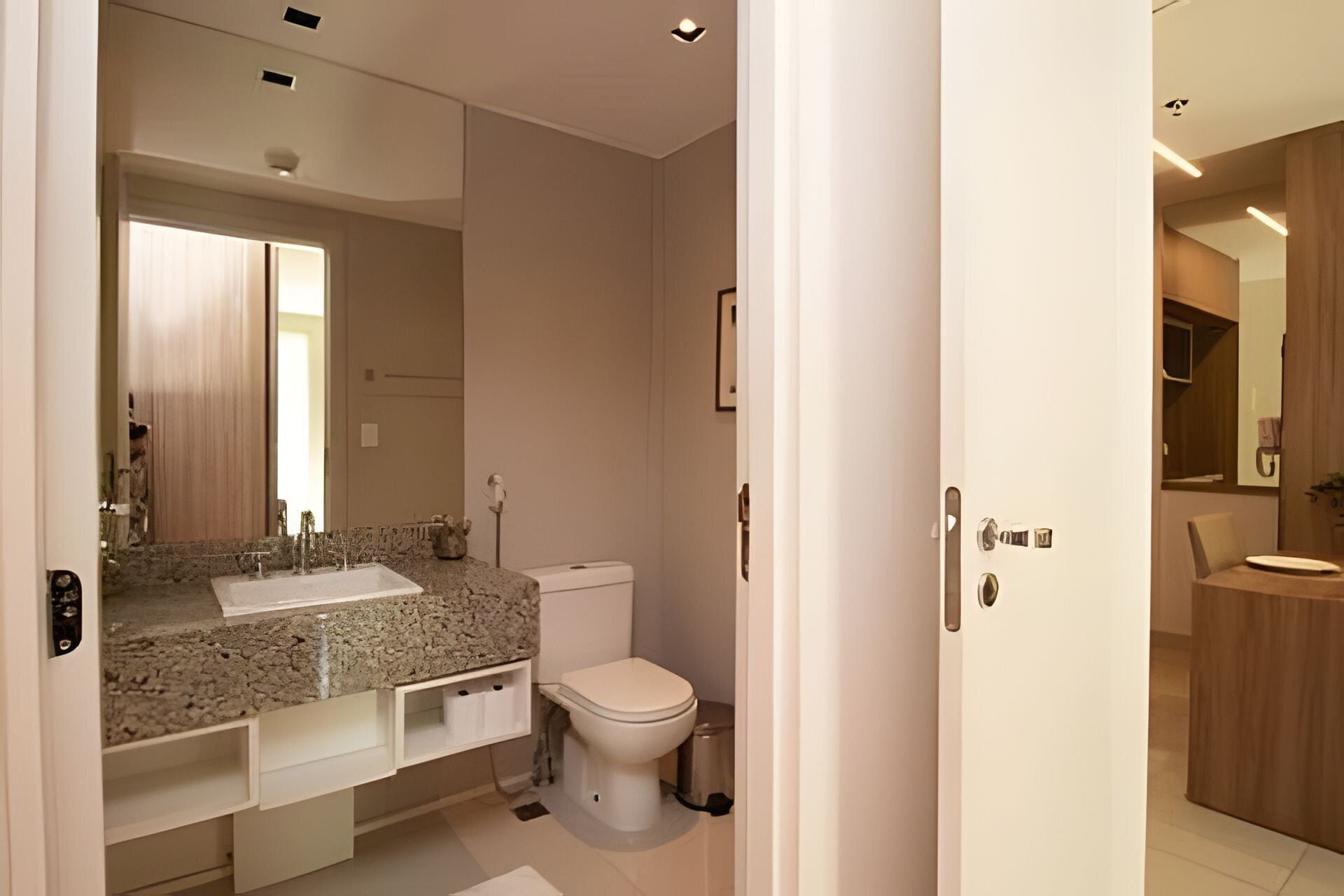 A modern bathroom with a granite countertop, a toilet, and a mirror.
