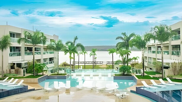 A modern hotel with a central pool, surrounded by palm trees and a view of the sea. -  OZPED Flats Particulares Brisas do Lago (Brasília)