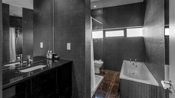 A modern bathroom with black tiled walls, a black sink, a white toilet, and a white bathtub.