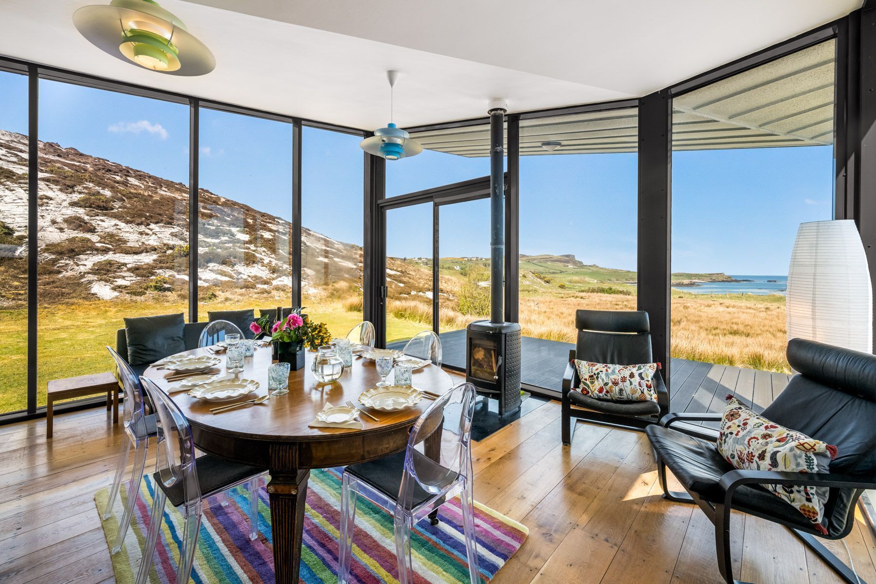 A dining area with a table set for four, large windows offering a view of a coastal landscape, and a modern interior design.