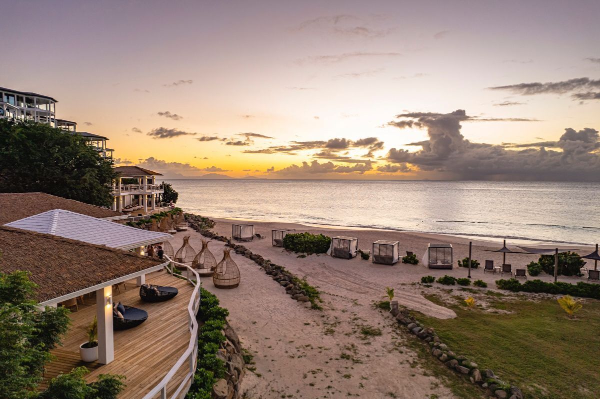 A beachfront property with a wooden deck, lounge chairs, and a view of the ocean at sunset.