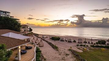 A beachfront property with a wooden deck, lounge chairs, and a view of the ocean at sunset.