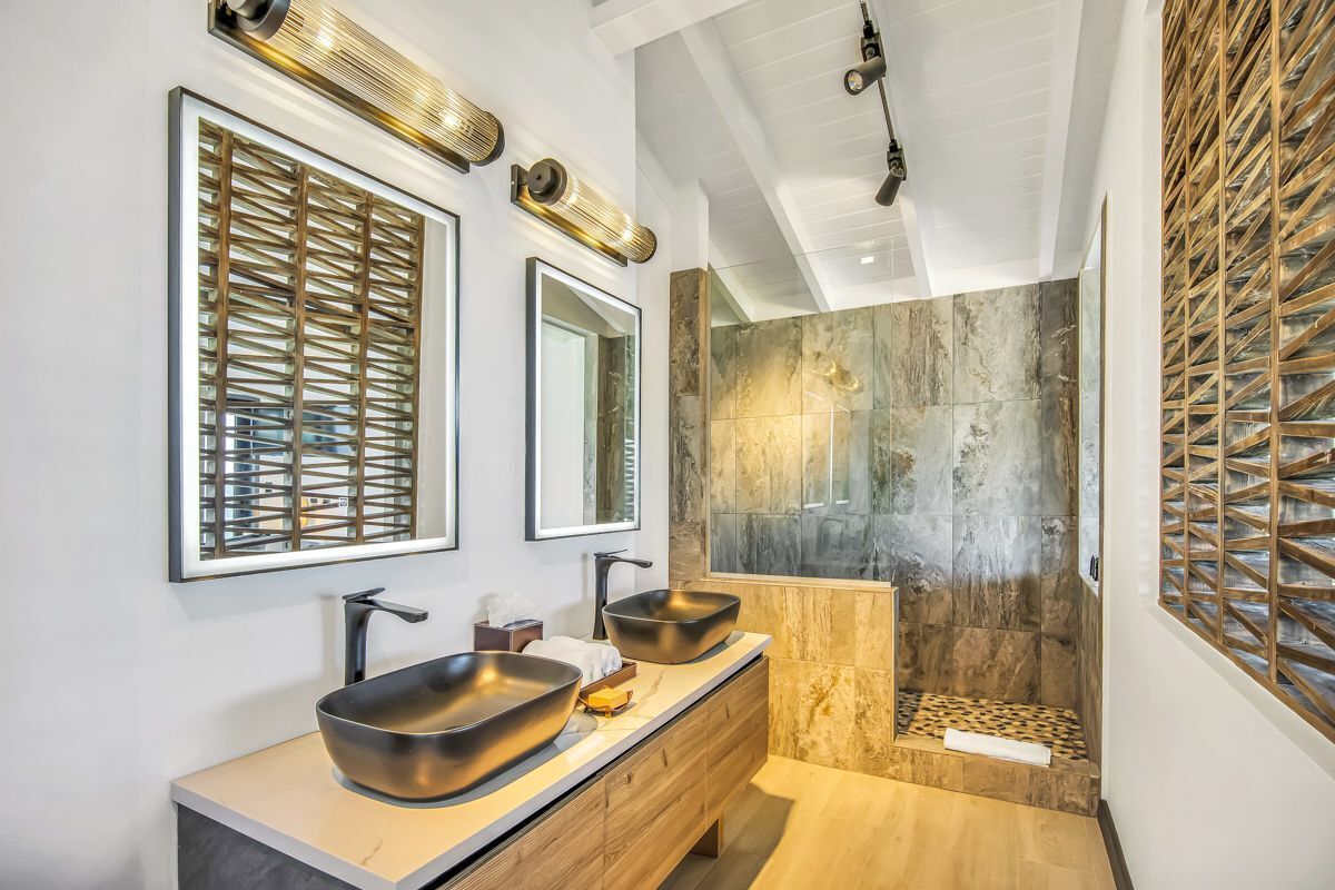 Un baño moderno con dos lavamanos de pedestal grandes, una ducha a ras de suelo con pared de piedra y un separador de madera celosía.