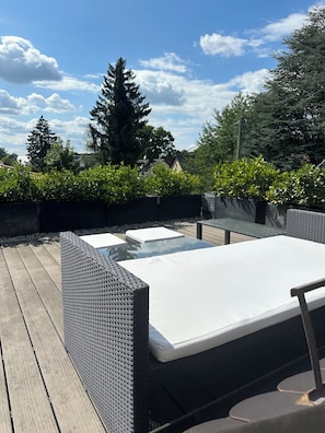 Eine Terrasse im Freien mit einem Tisch aus Glas und einer gepolsterten Bank.