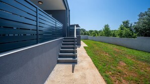 A modern building with a staircase leading to a covered area, surrounded by greenery and a clear sky. - Domus Alba Apartments - Apt 1 (Pula)