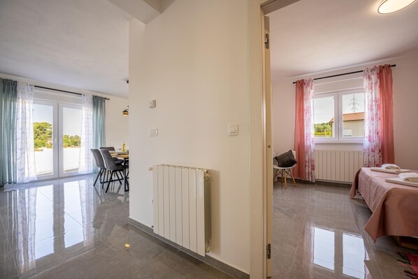 A modern hotel room with a large sliding glass door leading to a balcony, a neatly made bed, a small seating area, and a dining table with chairs. - Domus Alba Apartments - Apt 1 (Pula)