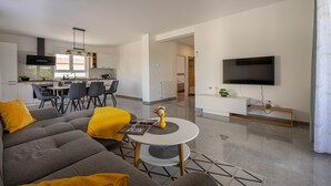 A modern living room with a grey sofa, yellow cushions, a round coffee table, and a flat-screen TV mounted on the wall. - Domus Alba Apartments - Apt 1 (Pula)