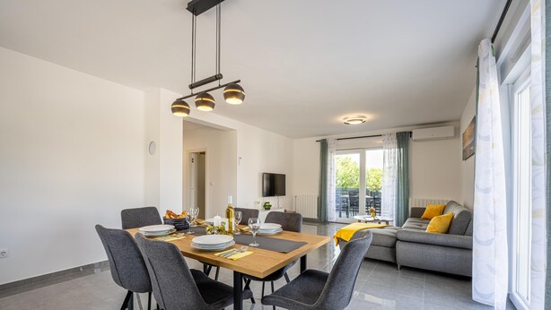 A modern dining area with a wooden table, grey upholstered chairs, and pendant lighting. - Domus Alba Apartments - Apt 1 (Pula)