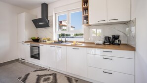 A modern kitchen with white cabinets, a black range hood, a window with a view, and a marble backsplash. - Domus Alba Apartments - Apt 1 (Pula)