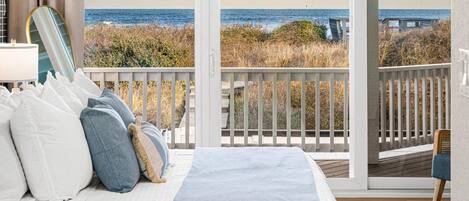 A bedroom with a large bed, a view of the ocean, and a balcony with a railing.