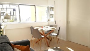 Una sala de estar moderna con una mesa de comedor, sofá gris y un ventanal que proporciona luz natural.