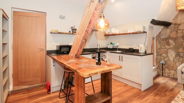 Una cucina con tavolo in legno, sgabelli da bar, lampadario e parete in pietra.
