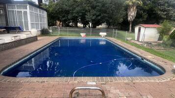 Relax by the pool surrounded by a brick patio and lush greenery.