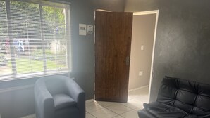 Ein Zimmer mit einem dunkelgrauen Sofa, einem passenden Hocker und einem Fenster mit Jalousien.