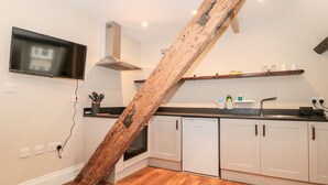 Una cocina con armarios blancos, una escalera de madera, un televisor de pantalla plana y piso de madera.
