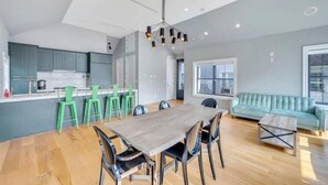 A modern kitchen with teal cabinets, a wooden dining table, and green chairs. - Villa Paraiso (Long Beach)