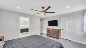 A bedroom with a bed, a ceiling fan, a TV, a wardrobe, and a bathroom door.