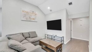 A modern living room with a grey sofa, a coffee table, and a flat-screen TV mounted on the wall.