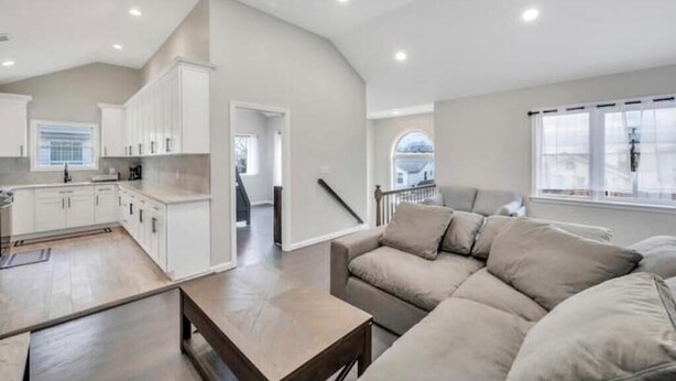 A spacious living area with a beige sofa, a wooden coffee table, and a kitchen with white cabinets.