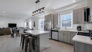 A modern kitchen with a central island, stainless steel appliances, and a dining area with a sofa and chairs. - Ocean Seabreeze (Long Beach)