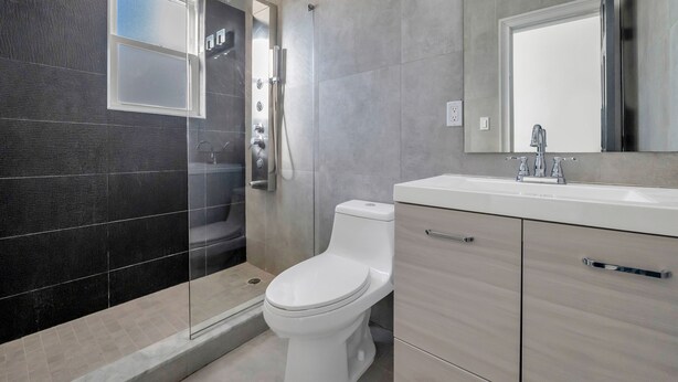 A modern bathroom with a glass-enclosed shower, a white toilet, and a large mirror above a sink with a faucet. - Ocean Seabreeze (Long Beach)