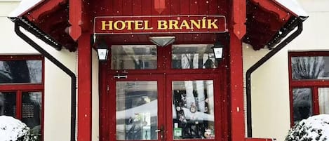 Um edifício de tijolos vermelhos com telhado coberto de neve e uma placa que diz 'HOTEL BRANIK'.