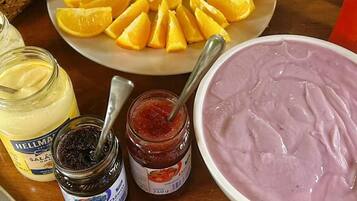 A table with a plate of sliced fruit, jars of condiments, and a bowl of pink food.