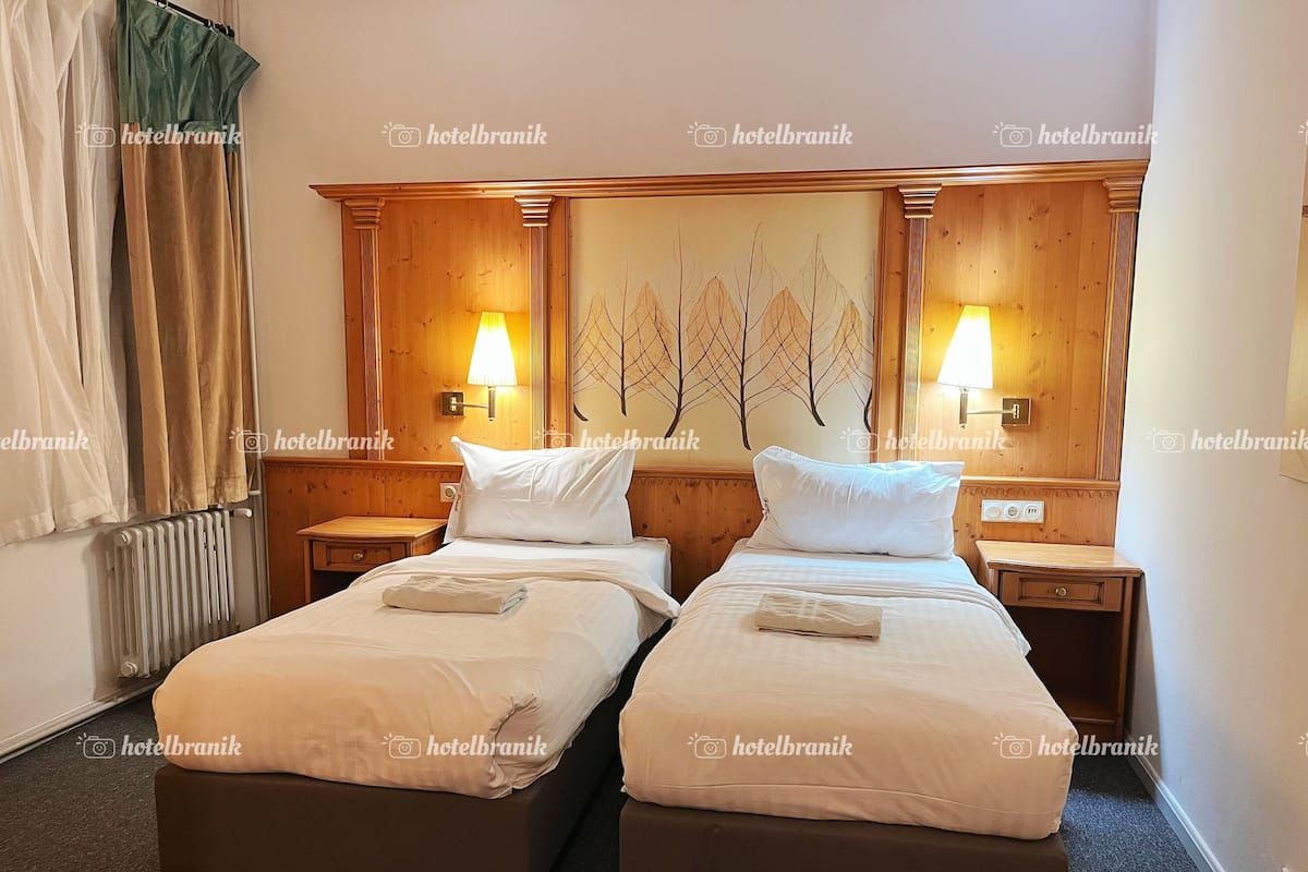 A hotel room with two single beds, a wooden headboard with a leaf mural, bedside lamps, and a radiator.