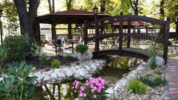 Un giardino con uno stagno, un ponticello di legno e un gazebo con posti a sedere all'aperto.