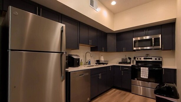 A modern kitchen with dark cabinets, stainless steel appliances, and a wooden floor. - Suites  On  Mass  -  C3 (Lawrence)