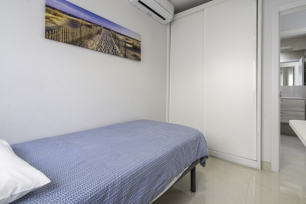 A bedroom with a single bed, a white door, and a painting on the wall.
