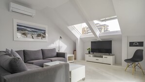 A modern living room with a grey sectional sofa, a white coffee table, a TV on a white cabinet, and a black chair. - Atico de dos Dormitorios con Terraza y Litera (Fuengirola)