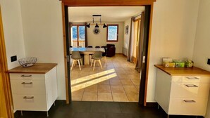 Una cocina luminosa con una mesa y sillas de madera, un armario blanco con cajones y una ventana que ofrece vistas a árboles.
