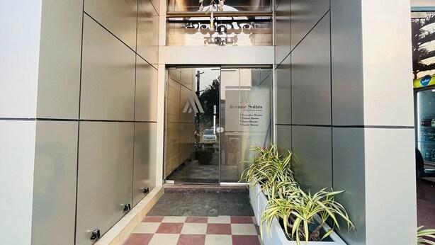 Entrada de hotel con piso a cuadros, una jardinera central con plantas y un candelabro.