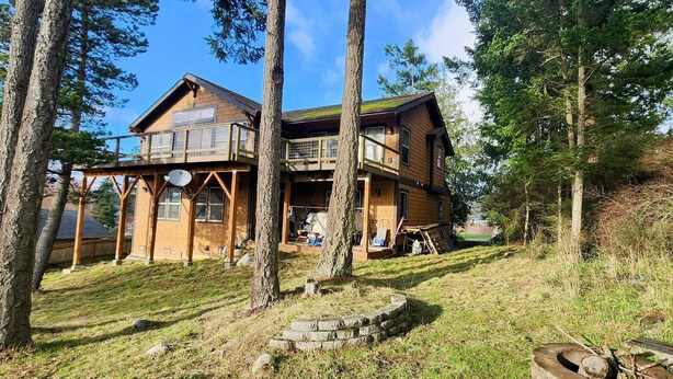 Eine zweistöckige Holzhütte mit Balkon, umgeben von Bäumen und einer Steismauer.