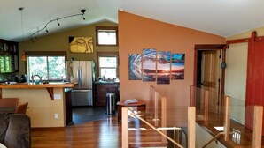 Eine moderne Küche mit einer zentralen Kochinsel, ein Essbereich mit einer Holztreppe und ein Wohnzimmer mit einer Couch.