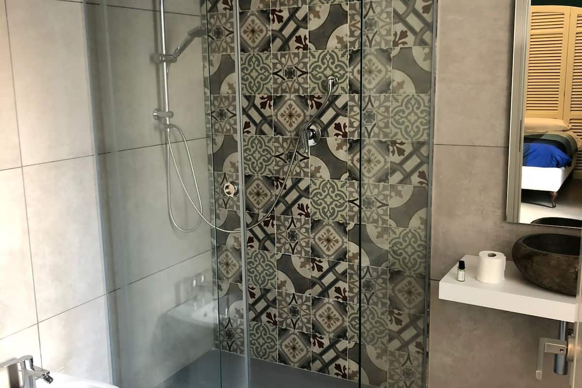 Un baño moderno con ducha envuelta en vidrio, un lavamanos pedestal blanco y un llamativo muro de azulejos.