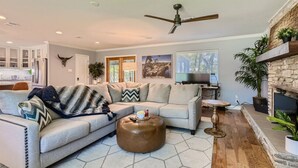 A modern living room with a sectional sofa, a round ottoman, a fireplace, and a ceiling fan. - Tesla Charger/Gorgeous Inside/Walk to Restaurants (Austin)