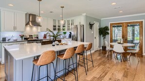 A modern kitchen with white cabinets, a large island with bar stools, stainless steel appliances, and pendant lighting. - Tesla Charger/Gorgeous Inside/Walk to Restaurants (Austin)