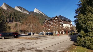 Un hotel de varios pisos con balcones, un estacionamiento y montañas al fondo.