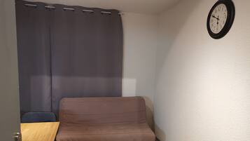 A small room with a brown sofa, a wooden table, a chair, and a wall clock.