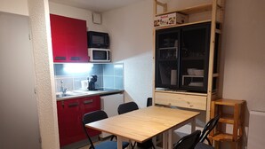 Una cocina compacta con un armario rojo, un microondas y una pequeña mesa de comedor con cuatro sillas.