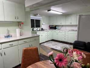 A kitchen with light green cabinets, a microwave, and a sink. There is a dining table with chairs and a vase of flowers.