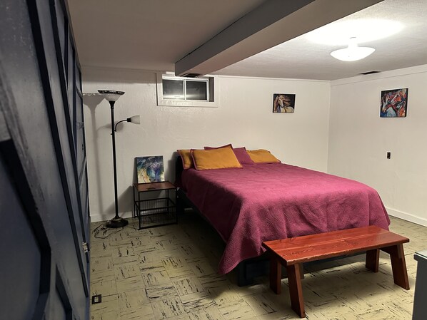 Une chambre à coucher avec un lit, un banc, une lampe sur pied et des œuvres d’art accrochées aux murs.