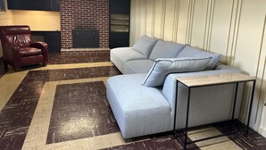 Ein Wohnzimmer mit einer Eckcouch, einem roten Ledersessel, einem kleinen Tisch und einem Boden mit Ziegeloptik.