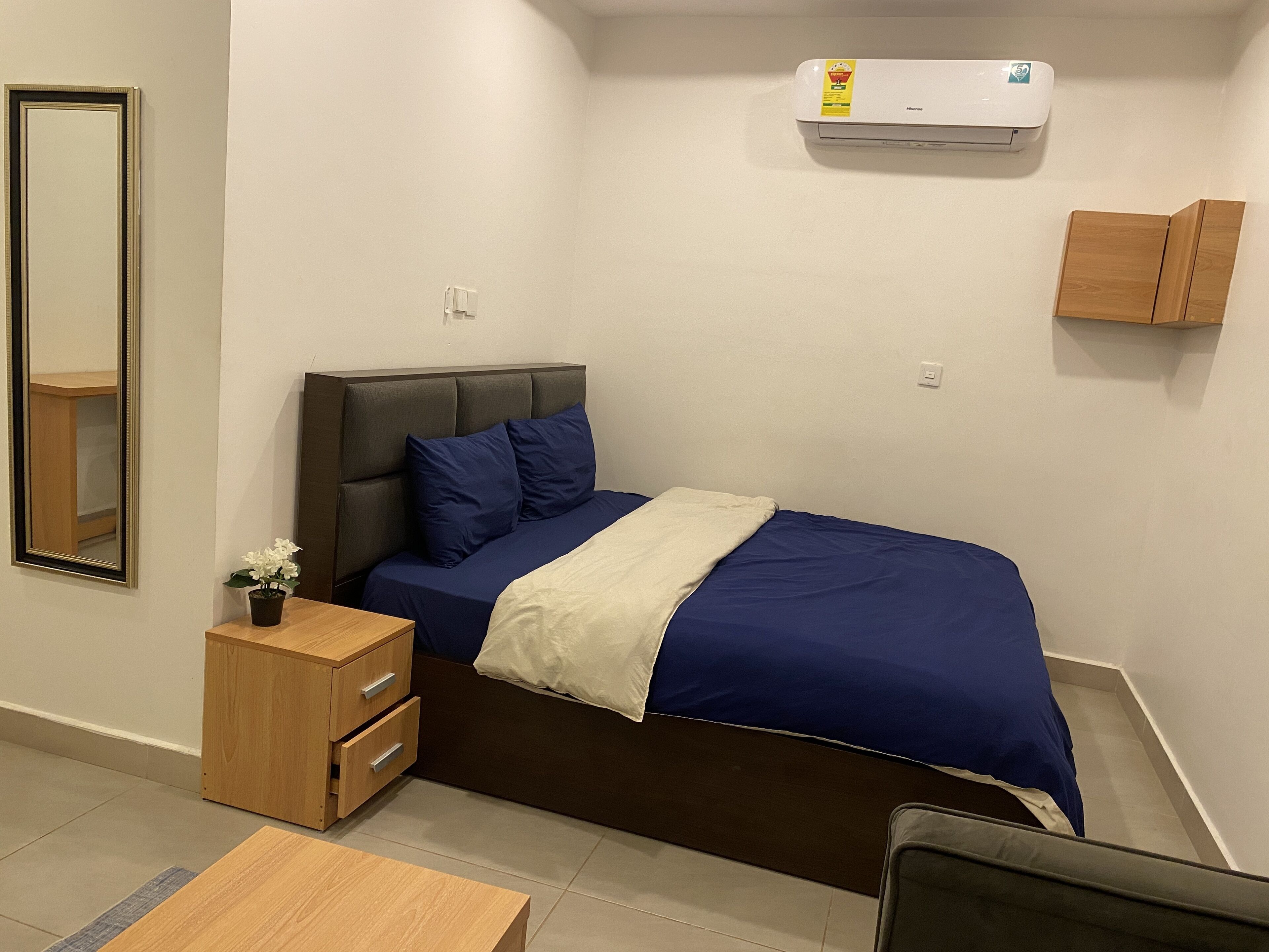 A bedroom with a bed, bedside table, mirror, and an air conditioning unit.