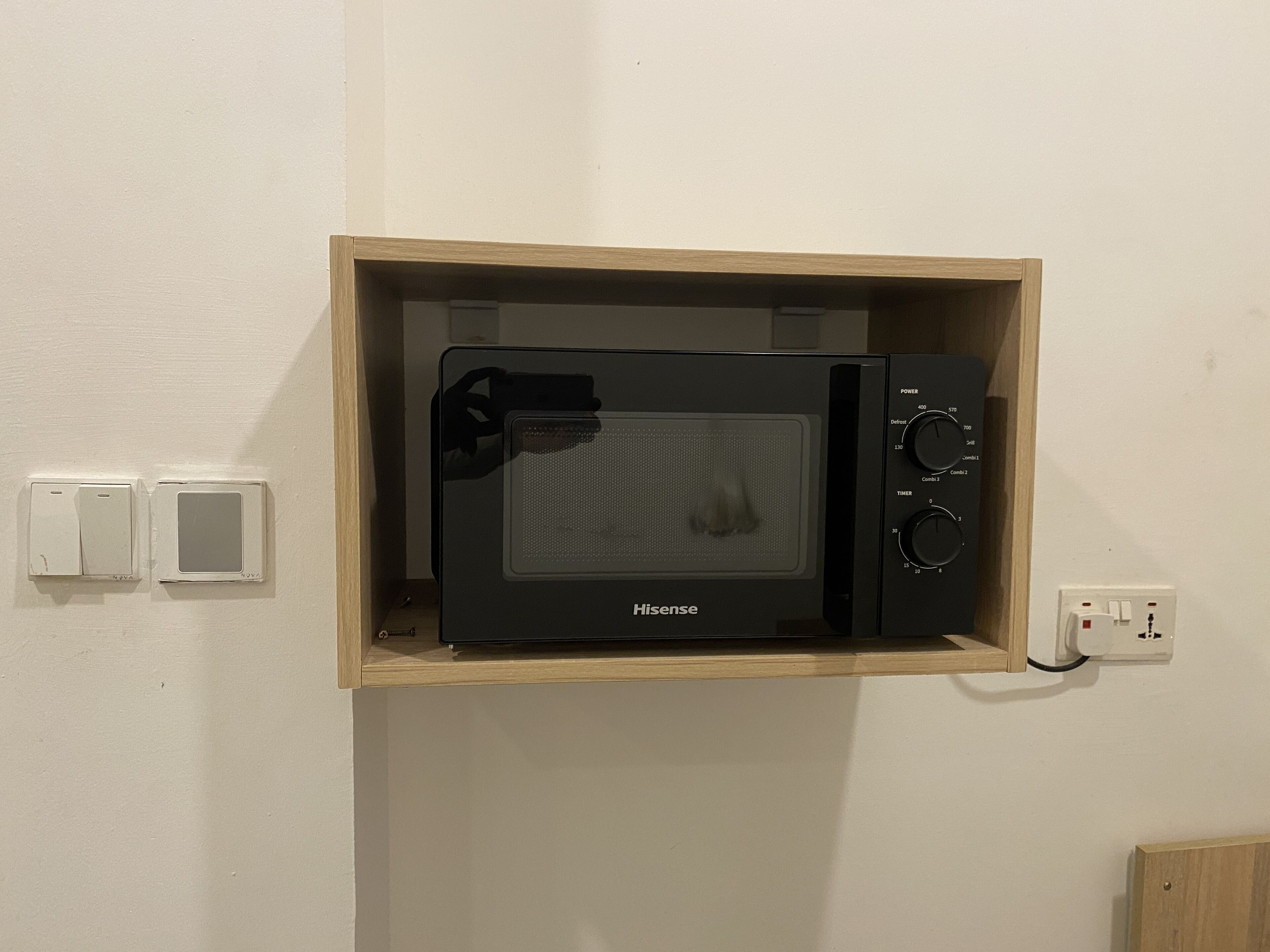 A Hisense microwave oven in a wooden cabinet with a power button, timer, and temperature control.