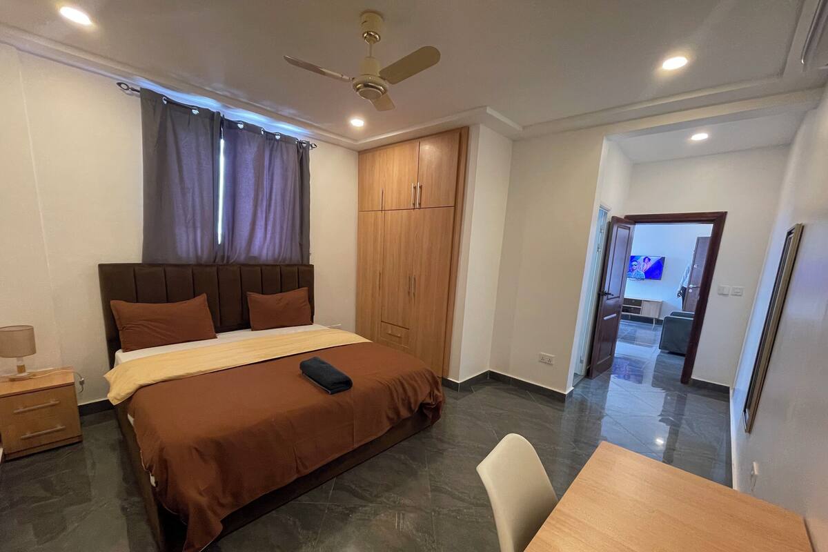 Une chambre à coucher comprenant un lit, une armoire en bois, un ventilateur de plafond et un coin repas avec une table et des chaises.