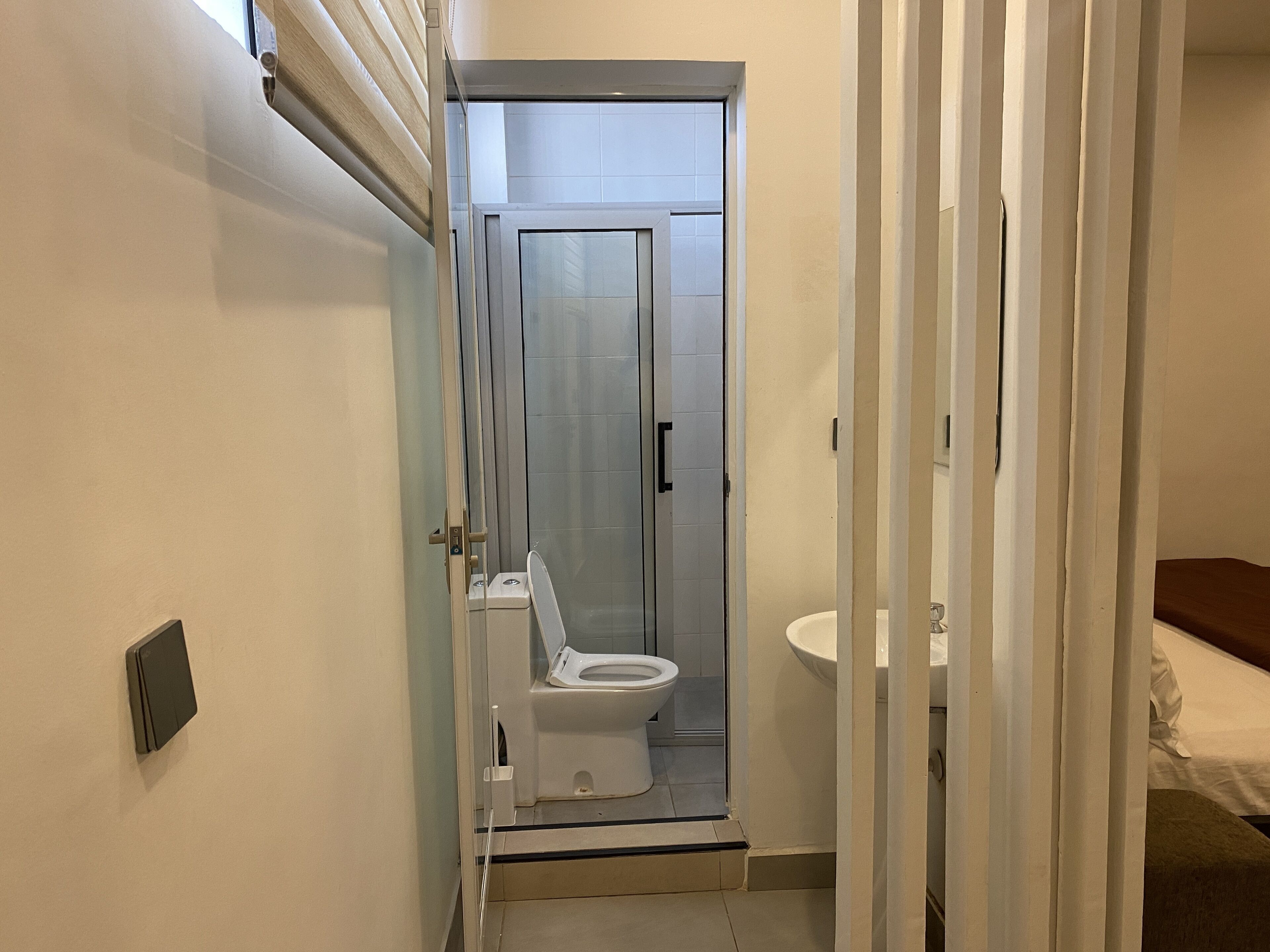 En smal hall som leder till ett badrum med toalett, handfat och en duschhörna.